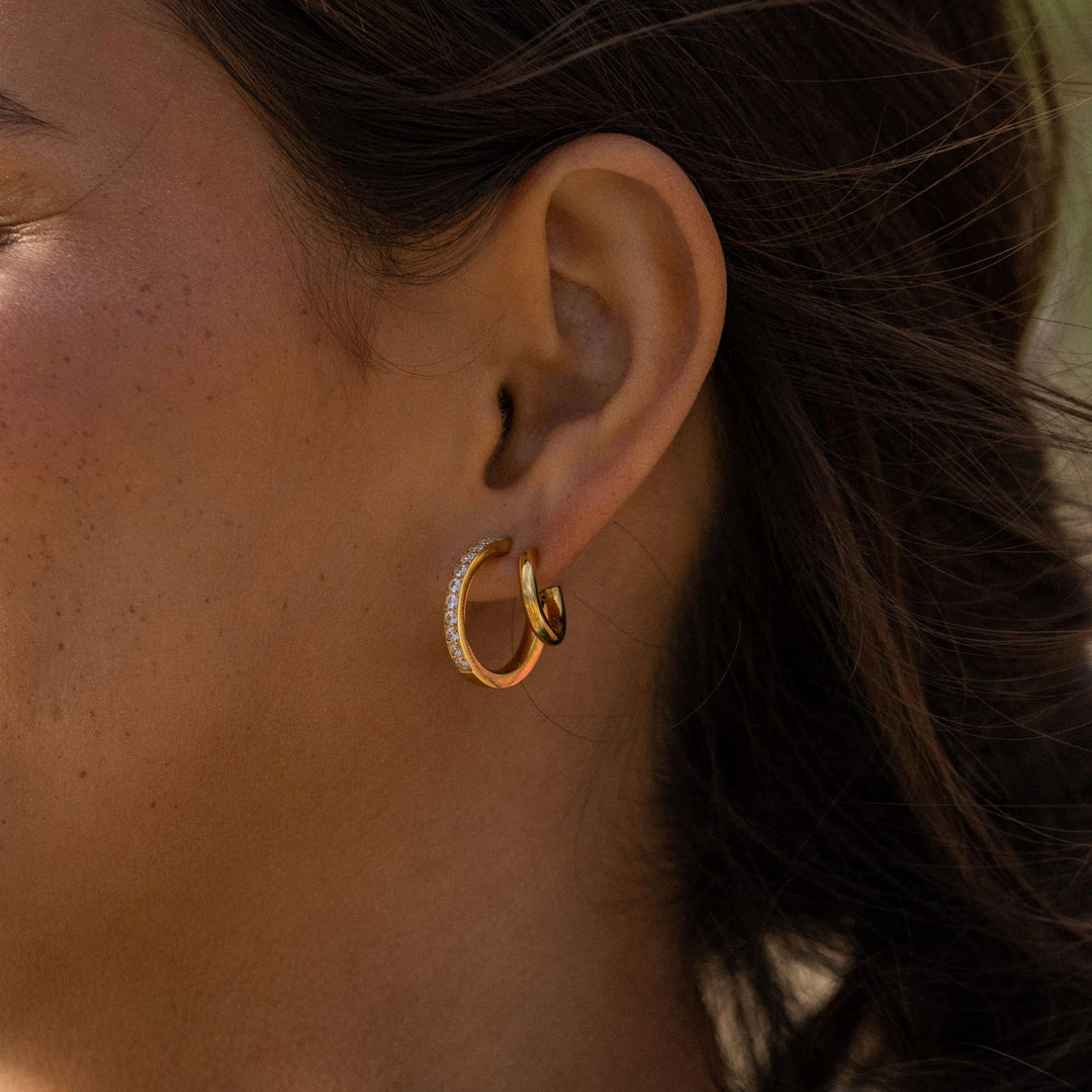 Gold Double Glitter Earrings by PURELEI on woman's left ear, adding radiant sparkle to her style.