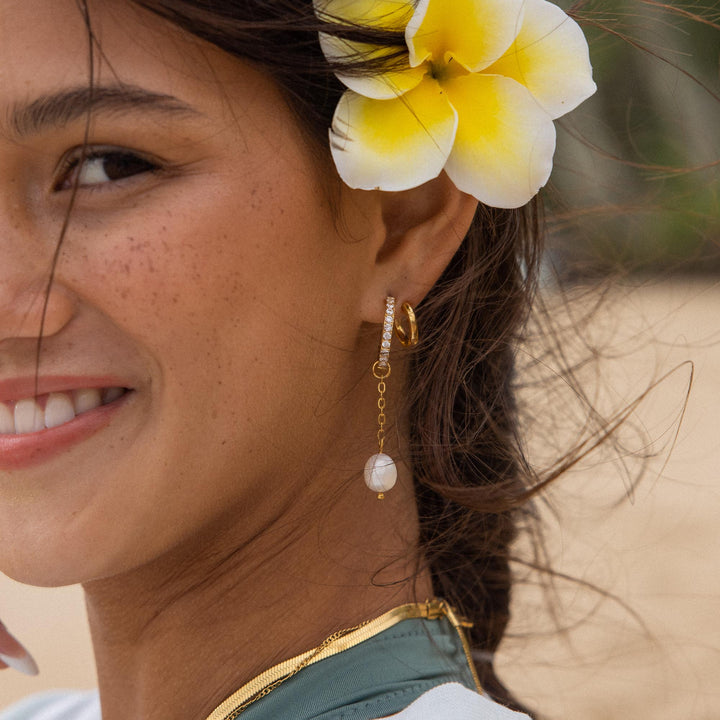 Gold double glitter earrings by PURELEI on a woman's left ear with a pearl-charm adding radiant sparkle to her style.