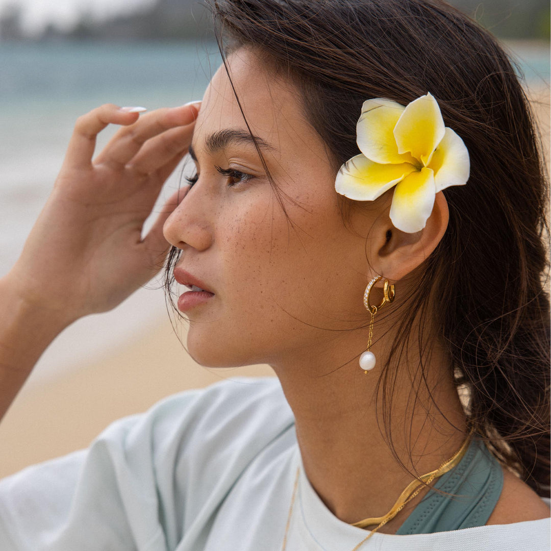 Gold double glitter earrings by PURELEI on a woman's left ear with a pearl-charm adding radiant sparkle to her style.