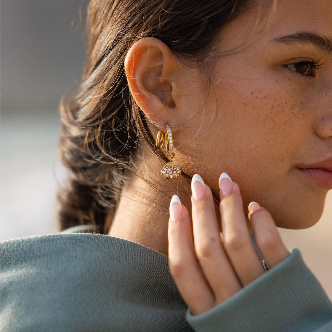 Gold double glitter earrings by PURELEI on a woman's right ear with a glitter charm to add a touch of sparkle to her style.