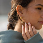 Gold double glitter earrings by PURELEI on a woman's right ear with a glitter charm to add a touch of sparkle to her style.