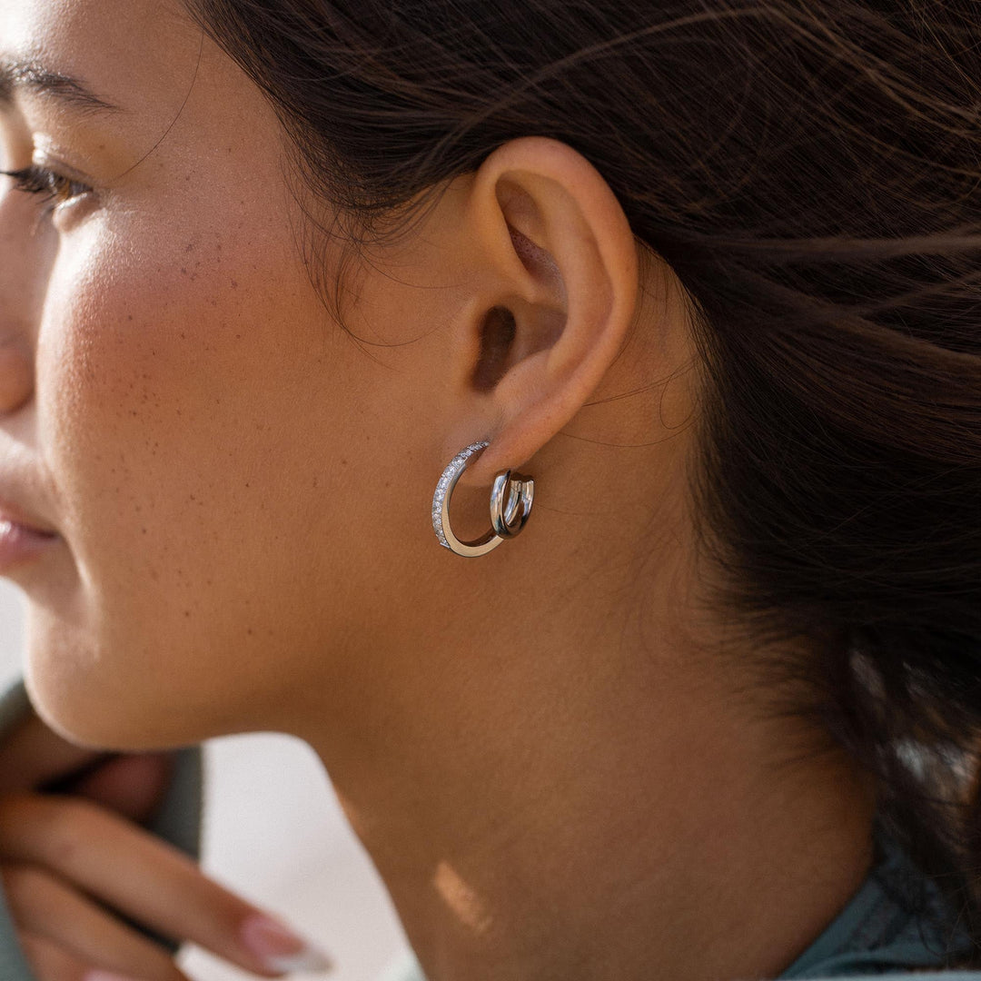 Silver double glitter earrings by PURELEI on a woman's left ear to add a touch of sparkle to her style.