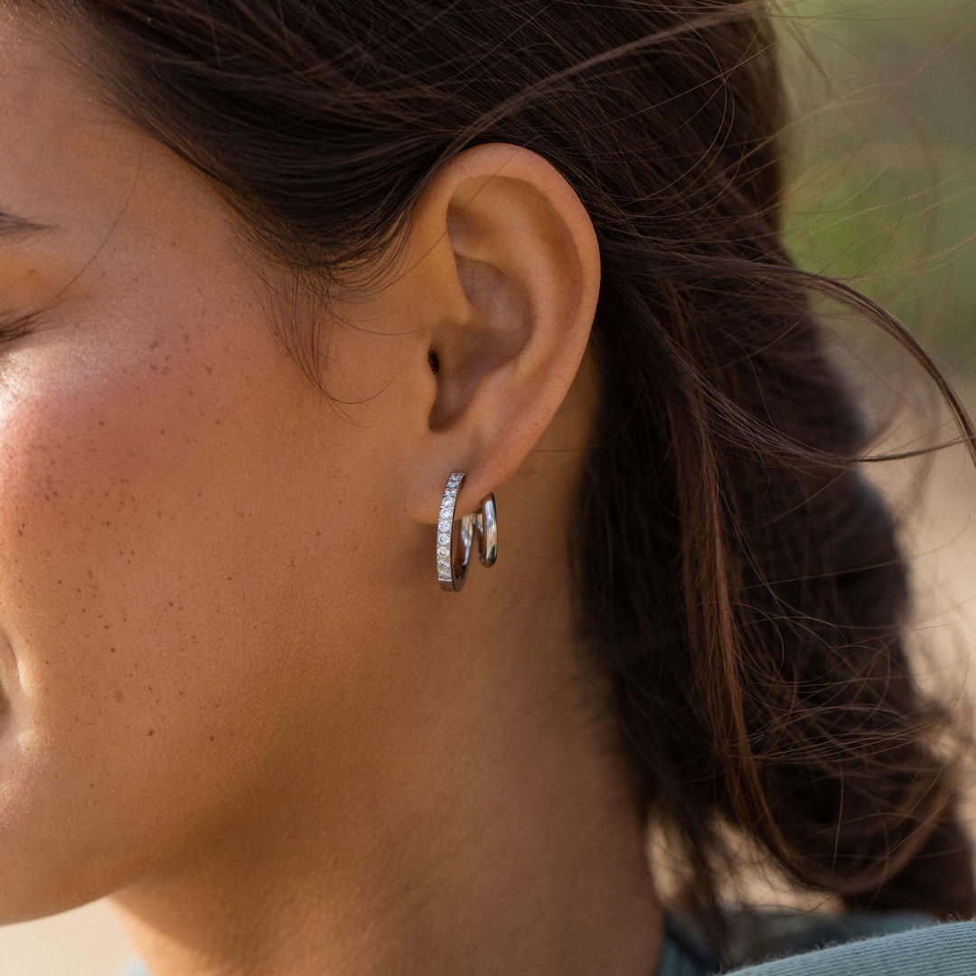 Silver double glitter earrings by PURELEI on a woman's left ear to add a touch of sparkle to her style.