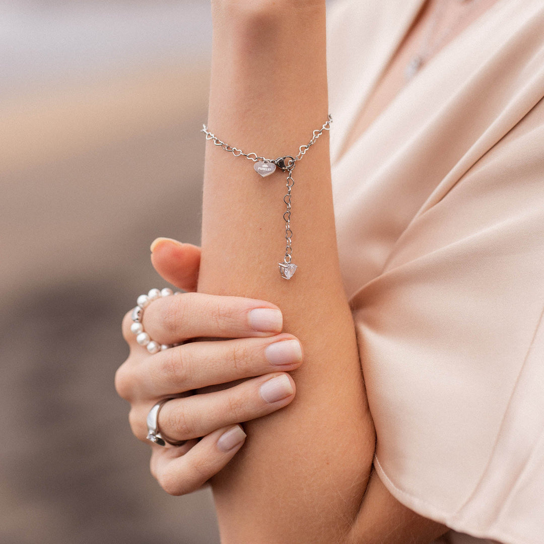 Woman wearing PURELEI Endless Love Bracelet on her left wrist, featuring silver heart-shaped links and a sparkling zirconia heart pendant.