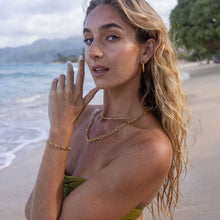 Woman at the beach wearing PURELEI’s gold Fashion Show Bracelet on her left arm and matching necklace.