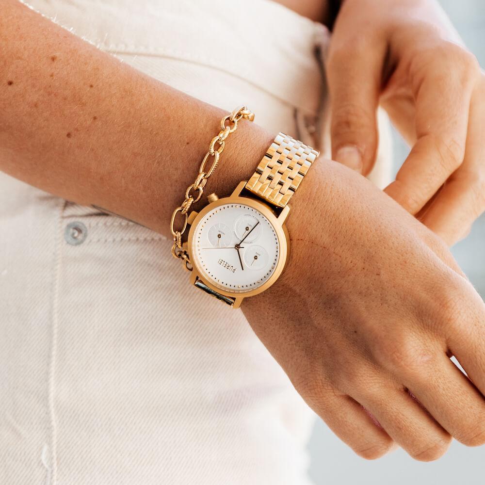 Close-up of a woman's right arm wearing PURELEI's gold Fashion Show Bracelet and a gold PURELEI watch.