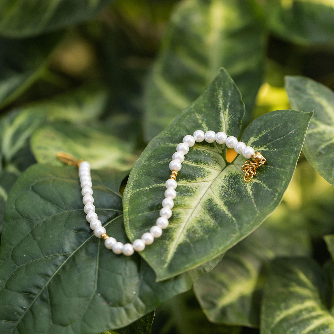 18K gold Finesse Bracelet by PURELEI with freshwater pearls elegantly placed on vibrant green leaves.