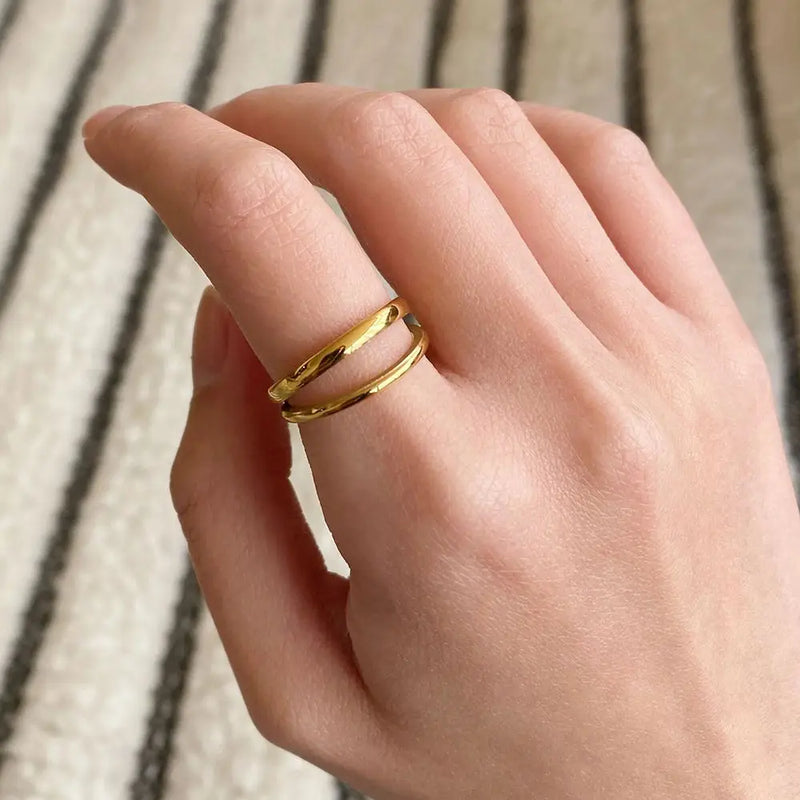 Goldener, offener Ring an Hand, minimalistisches Schmuckdesign auf gestreiftem Hintergrund