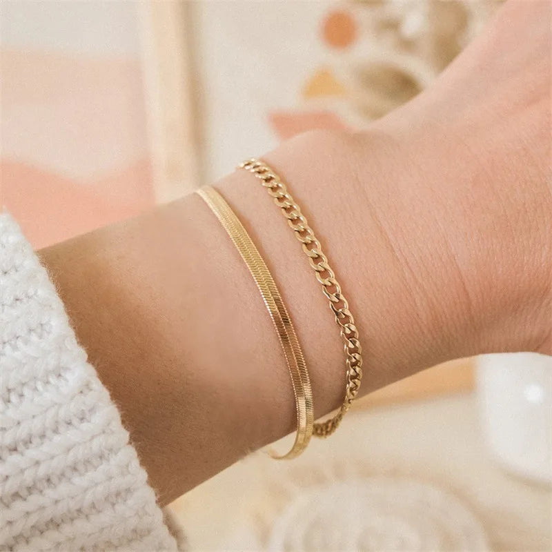 Zwei filigrane goldene Armbänder am Handgelenk, Nahaufnahme auf heller Oberfläche
