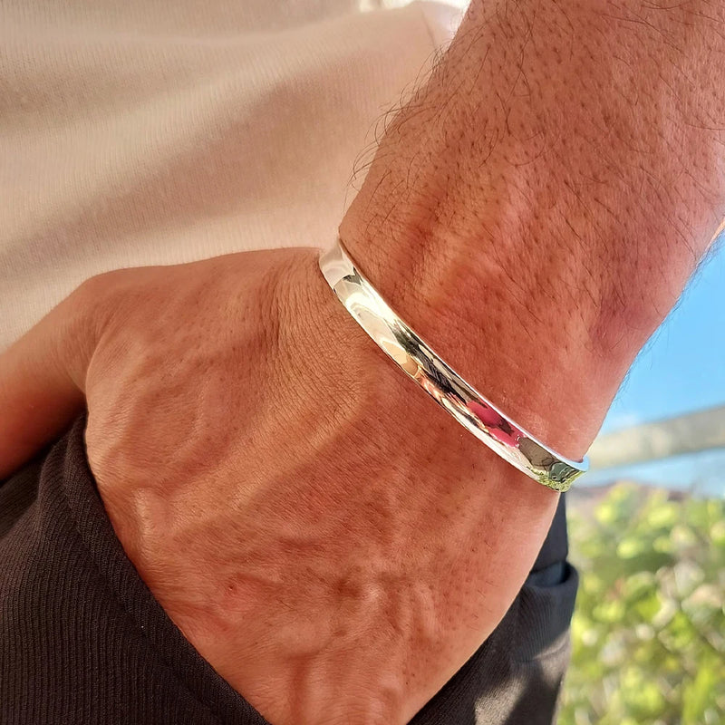 Herrenarm mit glänzendem Silberarmband, lässig getragen, Nahaufnahme im Sonnenlicht