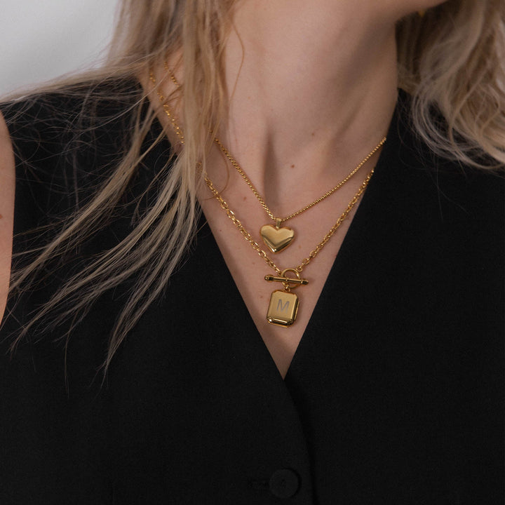 Woman wearing the PURELEI Lovebird Necklace in gold layered with another necklace, showcasing the shiny heart pendant elegantly.