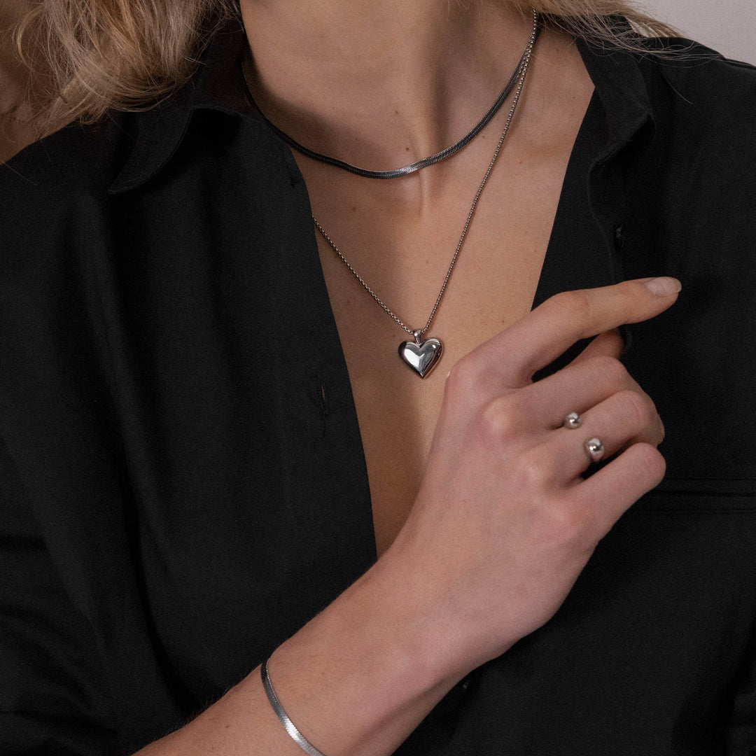 Woman wearing the PURELEI Lovebird Necklace in silver layered with another necklace, showcasing the shiny heart pendant elegantly.