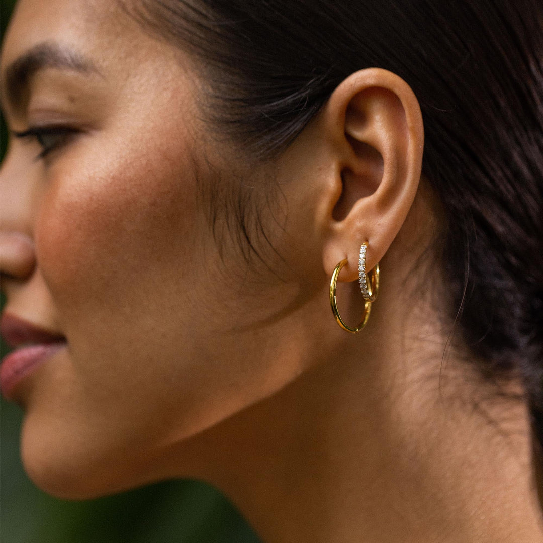 Woman wearing both pairs of PURELEI Lovely Glitter Earrings in gold on her left ear, showcasing elegance and sparkle.