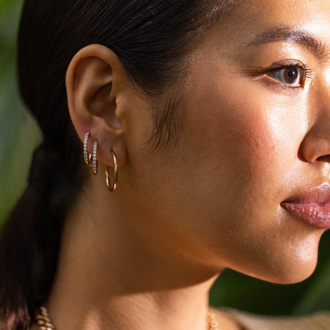 Woman wearing PURELEI Lovely Glitter Earrings on right ear: two hoops with zirconia and one plain gold hoop, styled elegantly.