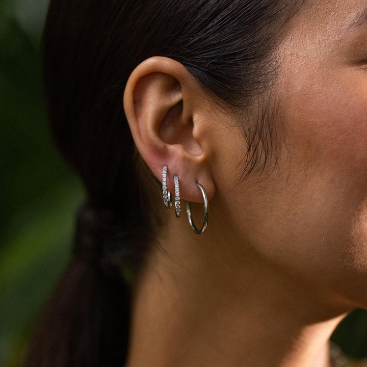 Woman wearing both pairs of PURELEI Lovely Glitter Earrings in silver on her right ear, showcasing elegance and sparkle.