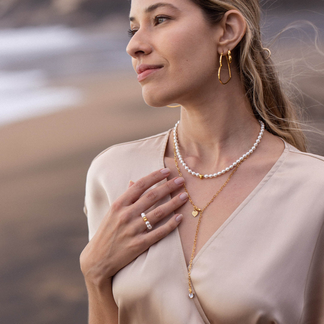 Woman layering the PURELEI Lovely Necklace in gold with another chain, showcasing the heart pendant and mixed pearls for a chic, elegant look.