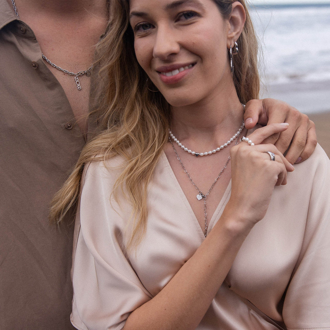 Woman wearing the PURELEI Lovely Necklace with mixed pearls and heart pendant layered with another necklace, standing beside her partner