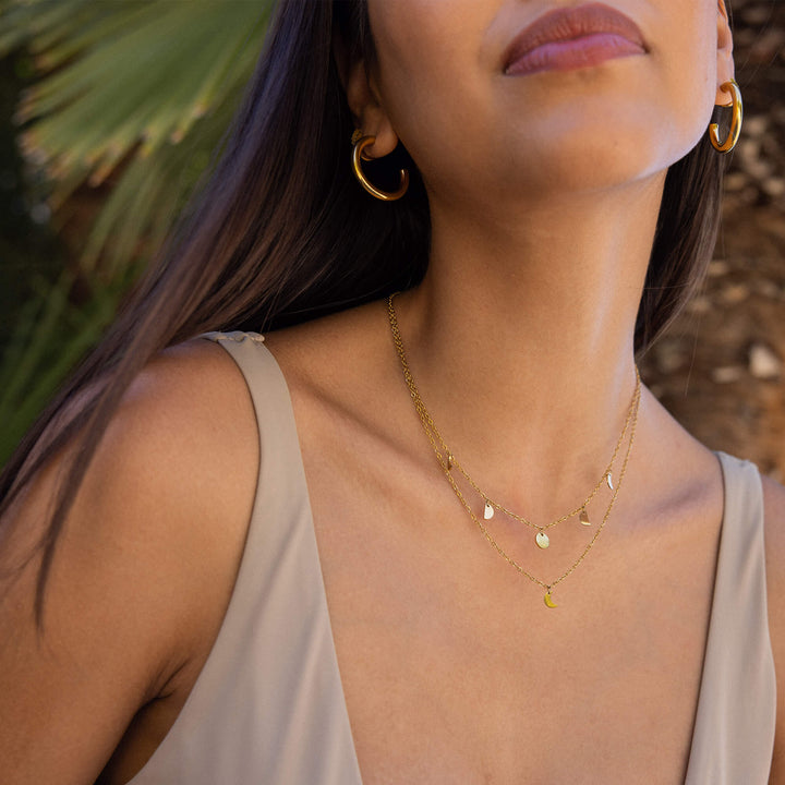 Woman wearing the PURELEI Luna gold necklace with delicate moon phase charms, elegantly showcasing its celestial design.