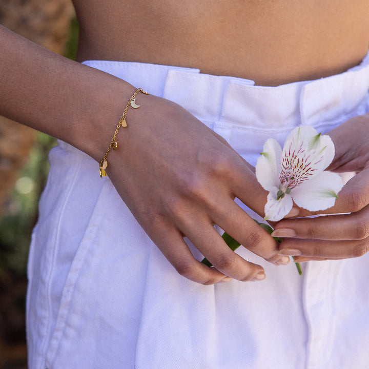 Woman wearing the PURELEI Luna bracelet in gold, showcasing delicate moon phase charms on her wrist in an elegant close-up.