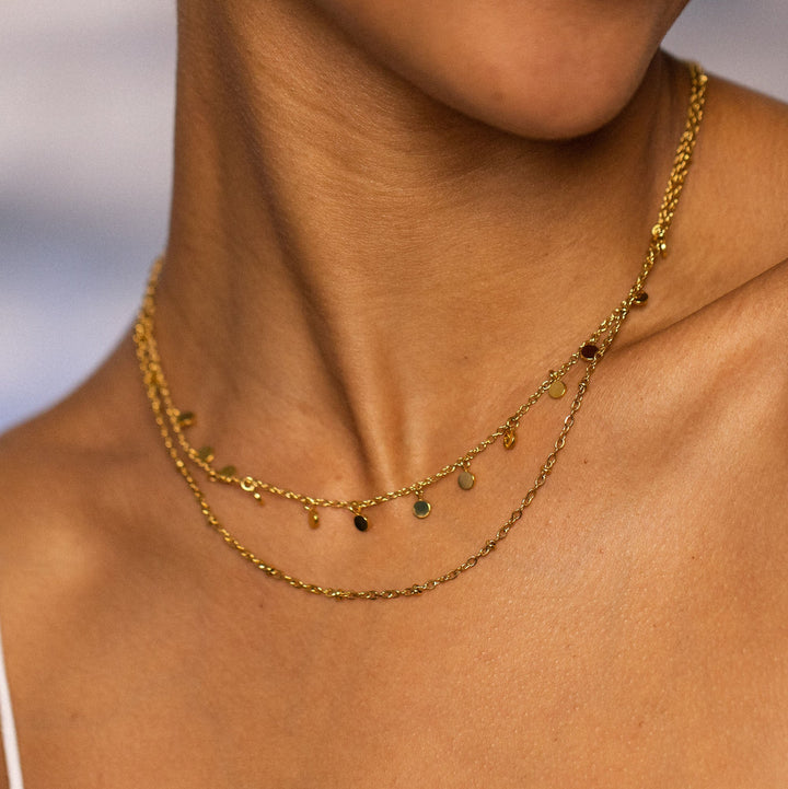 Woman wearing PURELEI Plain Necklace Gold: double-layered design with beads and coin pendants, adding elegance to her outfit.