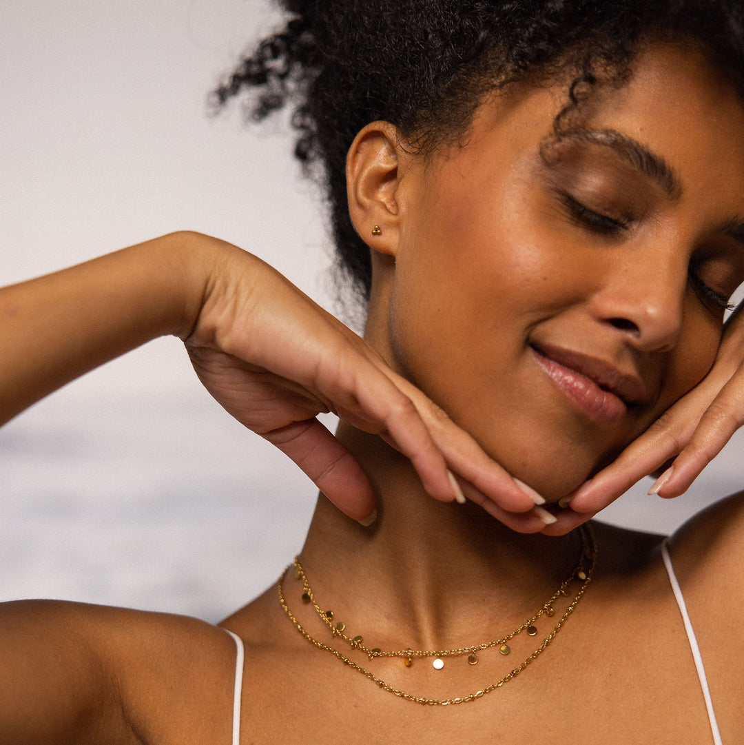 Woman wearing PURELEI Plain Necklace Gold: double-layered design with beads and coin pendants, adding elegance to her outfit.