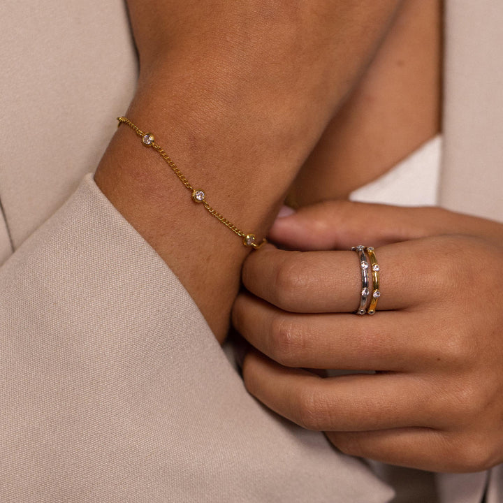 Woman wearing the PURELEI Spotlight Bracelet in gold on her right arm, paired with matching gold rings for an elegant look.